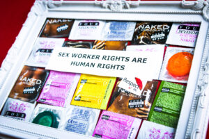 White picture frame on red background. Inside are colorful condoms with the text sex workers rights are human rights.