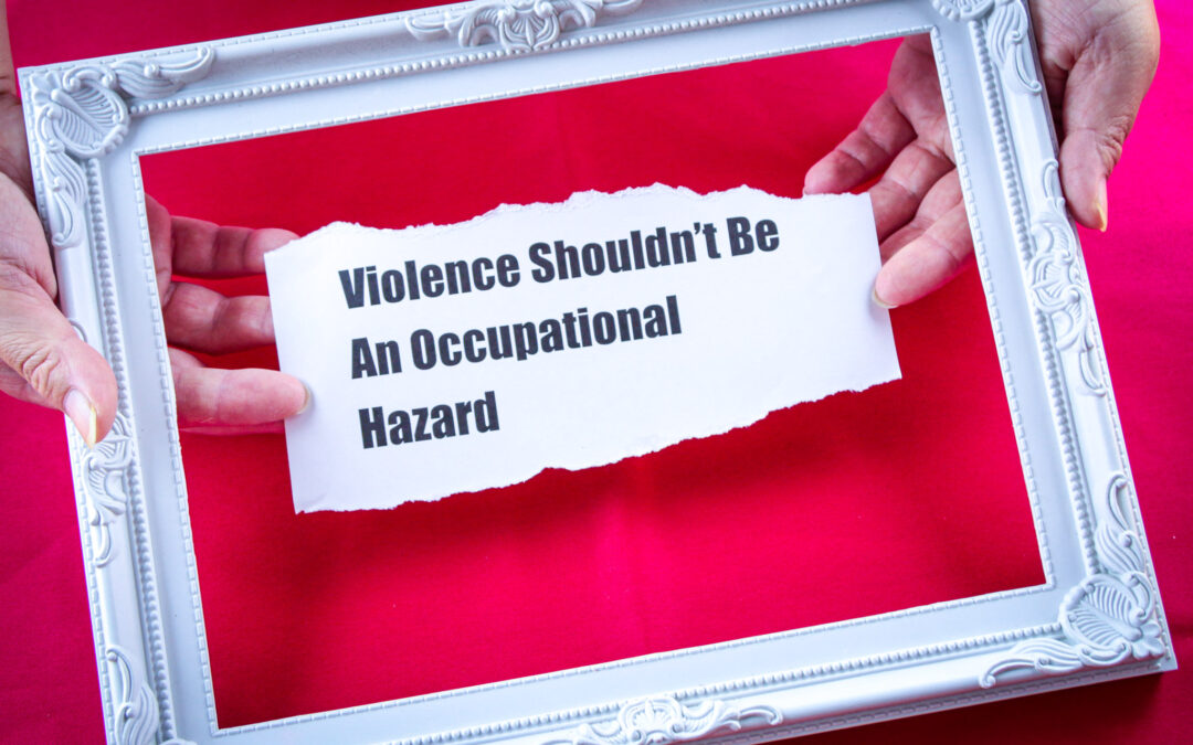White picture frame on red background. Inside two hands are holding torn paper with the text Violence should not be an occupational hazard