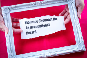 White picture frame on red background. Inside two hands are holding torn paper with the text Violence should not be an occupational hazard