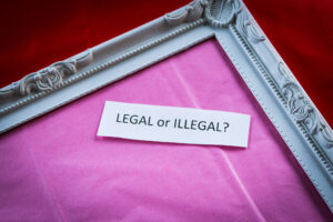 White picture frame on red background. Pink inside with cut out white paper. Written on the paper is Legal vs Illegal?